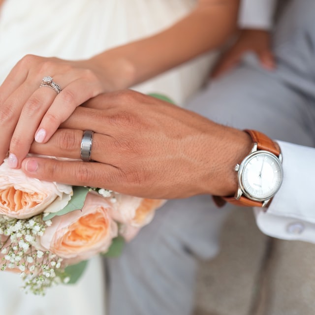 Newlyweds’ hands resting together, wedding bands and peach roses