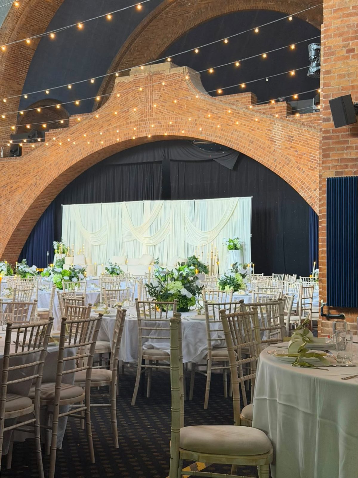 Ivory swagged stage backdrop with a plush sofa and lush green and white table centrepieces